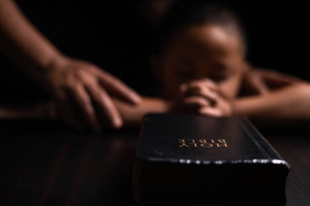 A Holy Bible in focus with a child praying in the background, symbolizing faith and guidance through Bible Digest.