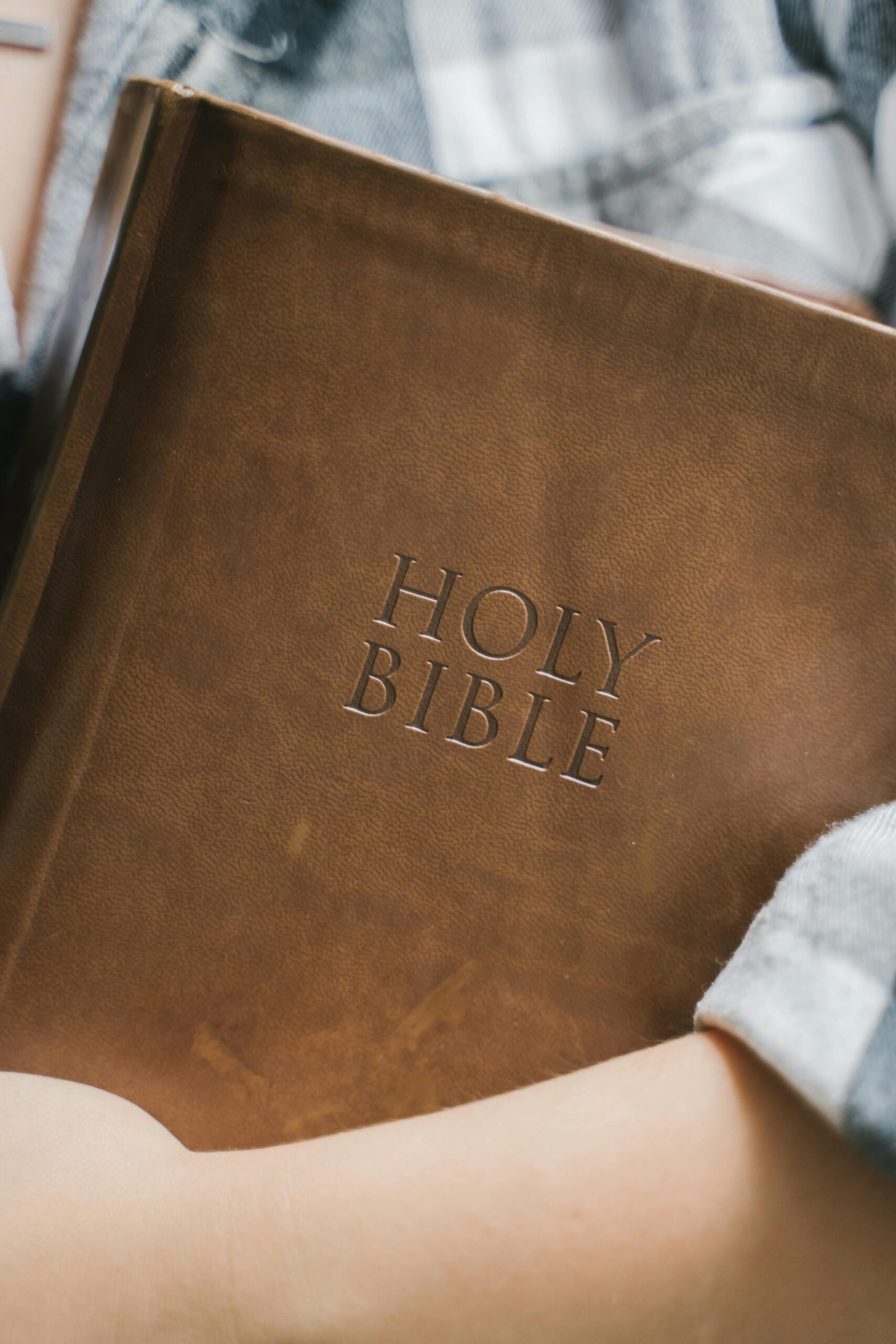 A close-up of a person holding a brown leather-bound Holy Bible, shared by Bible Digest to encourage thoughtful study and reflection.