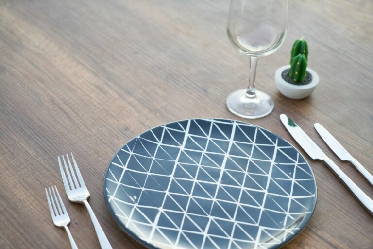 A minimalist table setting with a patterned plate, utensils, a wine glass, and a small cactus, shared by Bible Digest to illustrate spiritual reflection and gratitude during meals.