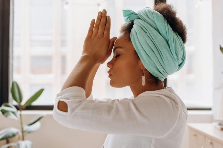 A woman in prayer with her hands pressed together, wearing a light turquoise headscarf, shared by Bible Digest to inspire faith and meditation.